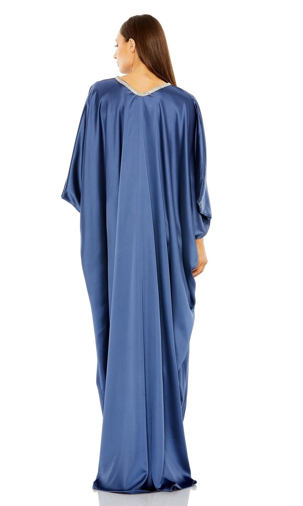 A woman stands facing away, wearing the Mac Duggal Long Formal Dress 27071—an ocean blue, loose-fitting, floor-length gown with draped sleeves and a V-shaped neckline.